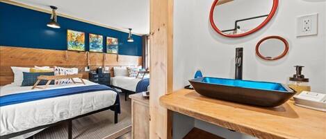 A bedroom with a wooden headboard, a bed with white bedding, a bedside table with a blue basin, and a wall-mounted mirror.