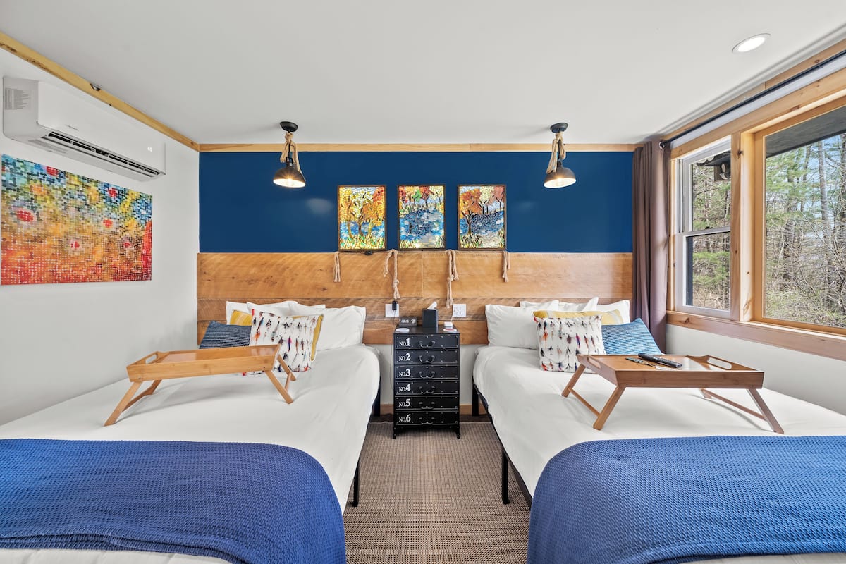 A hotel room with two beds, a wooden dresser, and a large window with a view of trees.