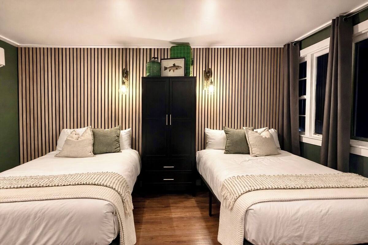 A room with two beds, a dark wardrobe, and a window with curtains.