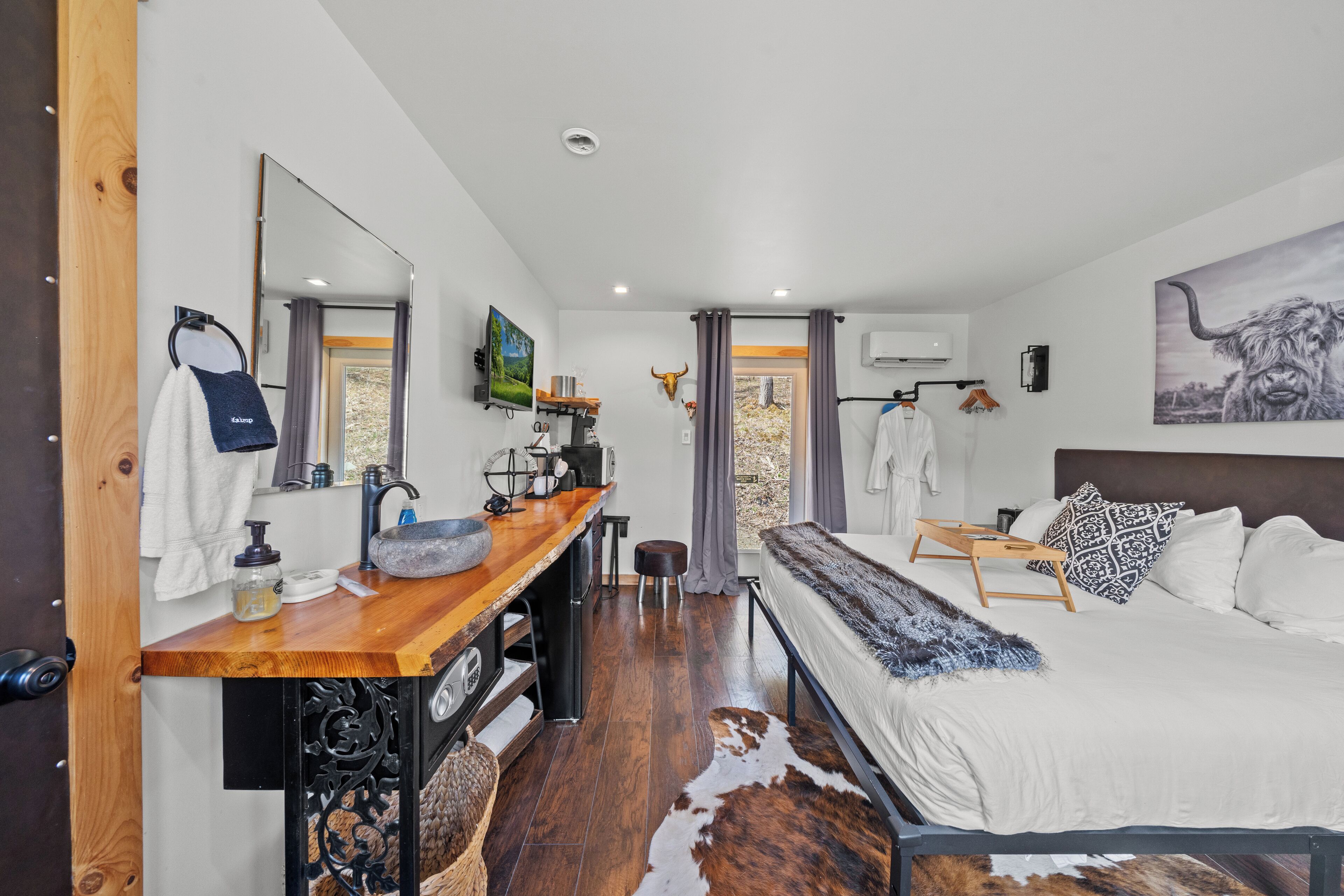 Un dormitorio moderno con un escritorio de madera, una cama grande, un espejo y un tapiz de cuero de vaca.