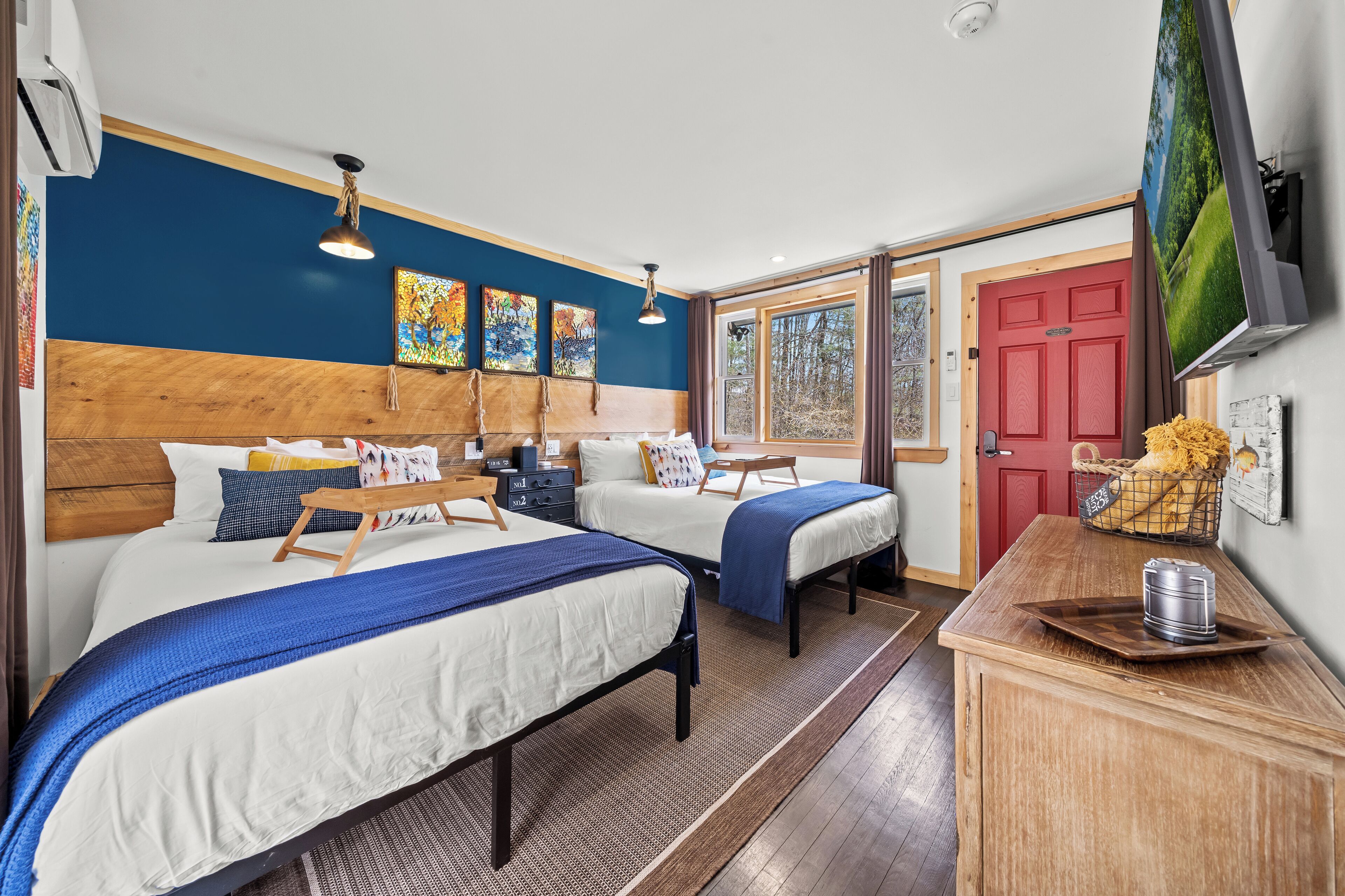 A hotel room with two beds, a wooden headboard, a TV, and a window with a view of trees.