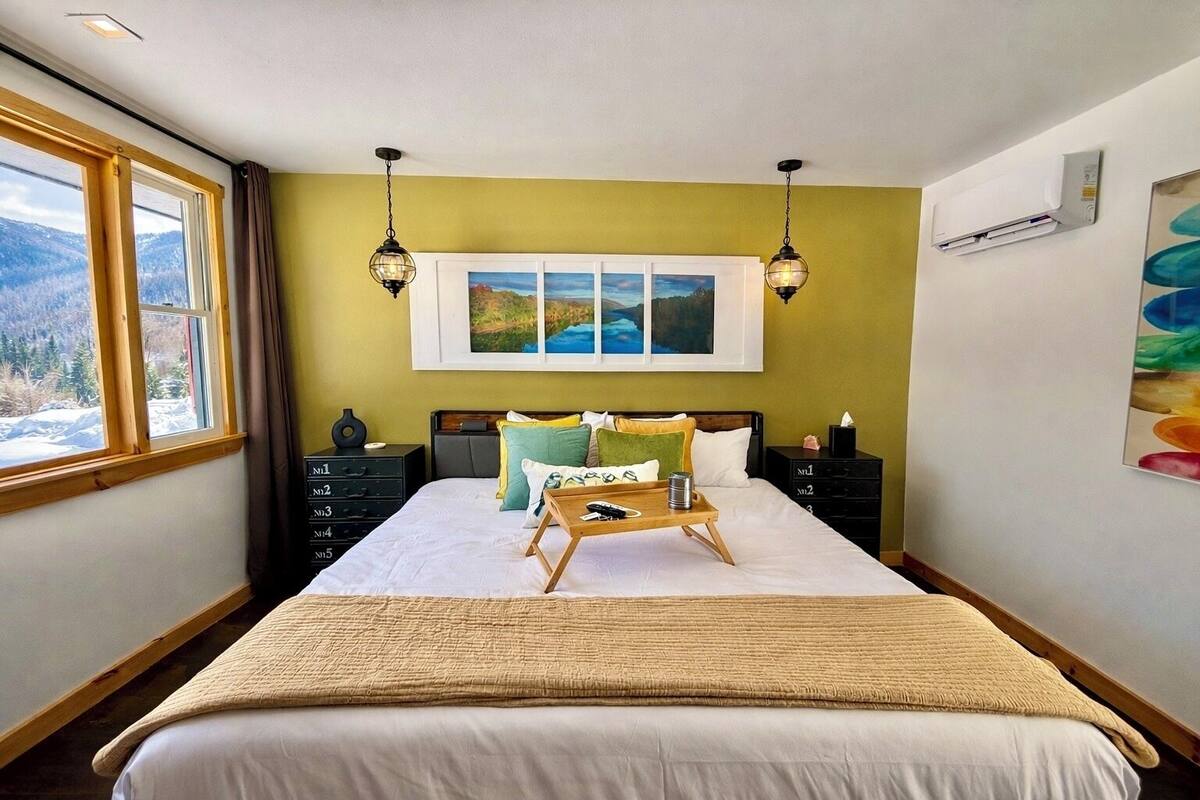 A bedroom with a bed, bedside tables, a window with a view, and a painting on the wall.