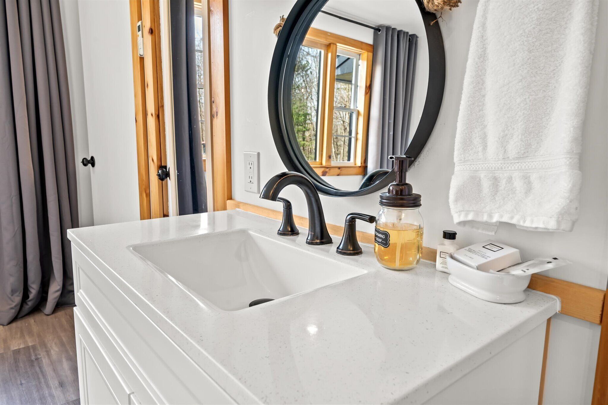 A bathroom with a white sink, black faucets, a round mirror, and a white towel hanging on the wall.