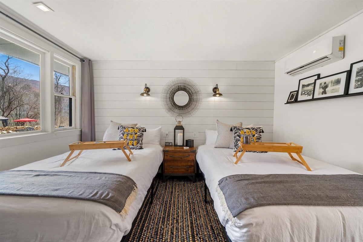 A room with two beds, a wooden nightstand, a mirror, and framed pictures on the wall.