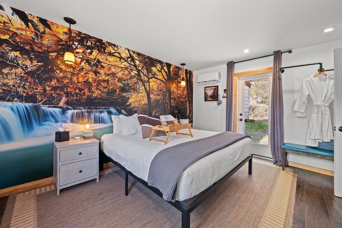 A bedroom with a bed, bedside table, and a large mural of a waterfall.