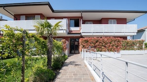 A two-story building with a balcony, a garden with various plants, and a clear sky.