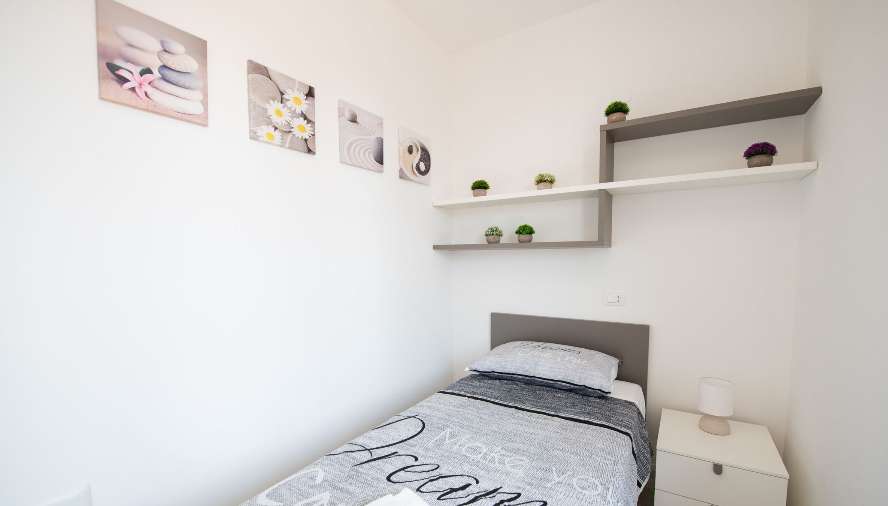 A minimalist bedroom with a bed, bedside table, and wall-mounted shelves with small plants.