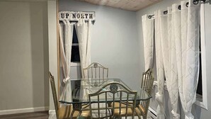 A dining area with a glass table and metal chairs, wooden ceiling, and white curtains.