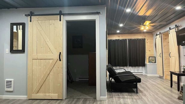 A room with a sliding barn door, a reclining chair, a ceiling fan, and a wooden table.