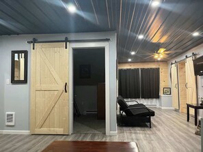 Een kamer met een schuifdeur van hout, een ligstoel, een plafondventilator en een houten tafel.
