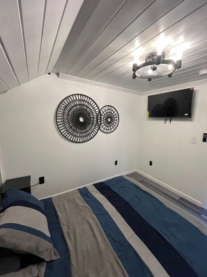 Un dormitorio con cama, televisor montado en la pared y dos cuadros.