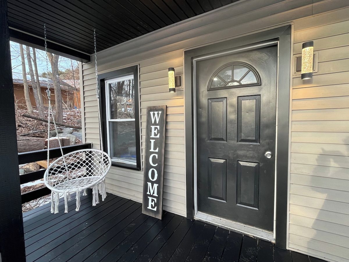 A porch with a swing chair, a 'WELCOME' sign, and a dark door.
