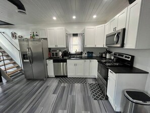 A modern kitchen with white cabinets, stainless steel appliances, and a grey patterned floor. - Lakefront Home w/ Dock & Fire Pits (Northville)