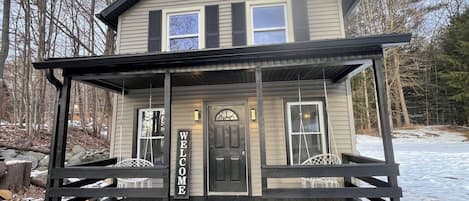 A two-story house with a porch, a welcome sign, and a door.