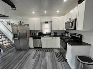 Una cocina compacta con armarios blancos, electrodomésticos de acero inoxidable y una alfombra estampada.