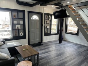 Un interior moderno con una escalera, una puerta gris y una mesa de madera.