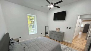 Ein Schlafzimmer mit einem Bett, einer Kommode, einem an der Wand montierten Fernseher und einem Deckenventilator.