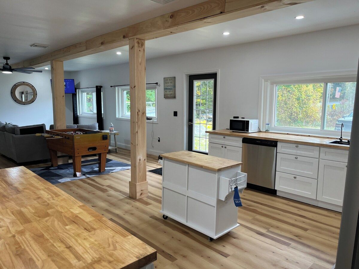 Une cuisine spacieuse avec un plancher en bois, une table de baby-foot, un chariot de cuisine et un lave-vaisselle.
