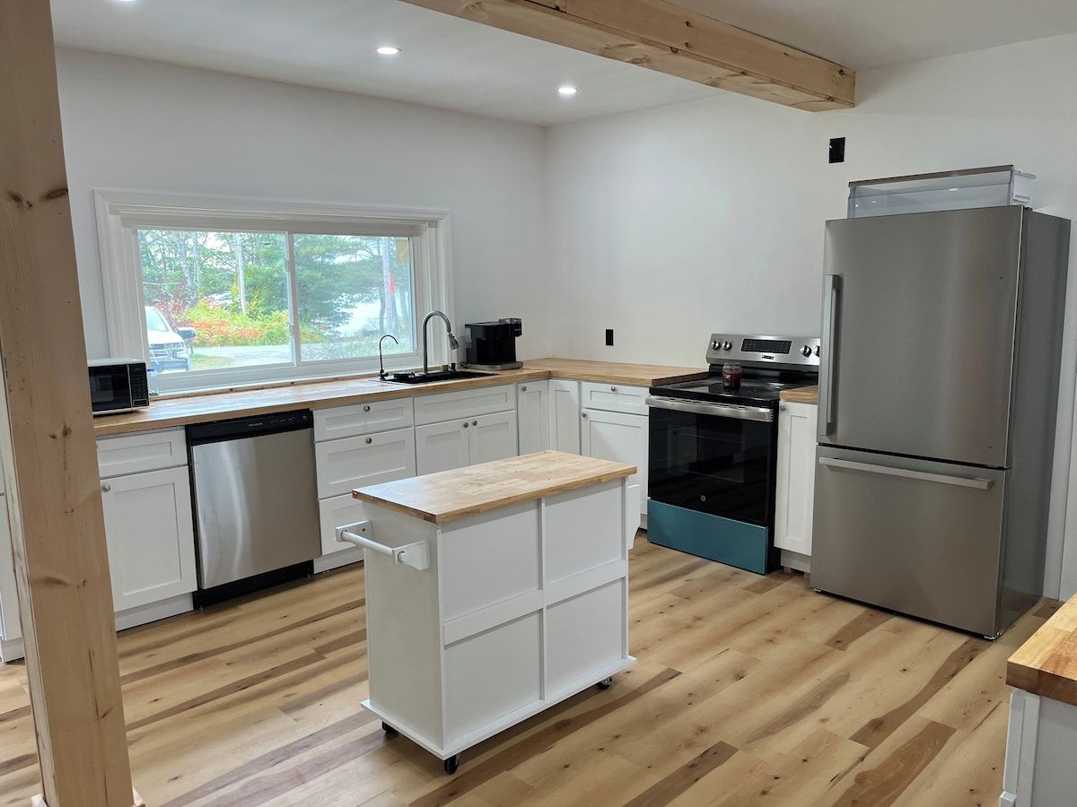 Une cuisine moderne avec des meubles blancs, un réfrigérateur en acier inoxydable et un plan de travail en bois.