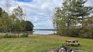 Ein Picknickplatz mit Tisch und Bänken, umgeben von Bäumen und Blick auf einen See.