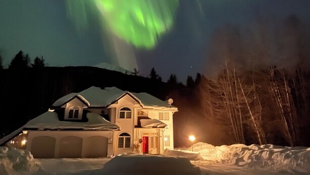 A house with a red door and garage, surrounded by snow, under a night sky with green aurora lights. - “Wake Up by the Lake — Private Alaska Stay Near Hiking & ATV Trails” (seward)
