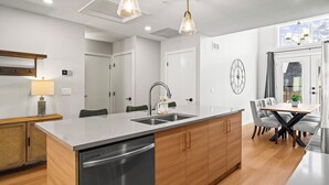 A modern kitchen with a central island, stainless steel appliances, and a dining area with a wooden table and chairs.