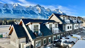 A row of modern buildings with a mountain backdrop, featuring a cross, parking area, and a clear sky.