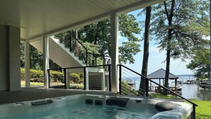Un jacuzzi con vistas a un lago, rodeado por una terraza cubierta y una escalera que lleva a un área techada.