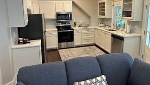 Una cocina moderna con armarios blancos, electrodomésticos de acero inoxidable y un sofá gris en primer plano.