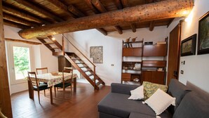 Una sala de estar acogedora con una escalera de madera, una mesa de comedor con sillas, un sofá con cojines y una estantería.