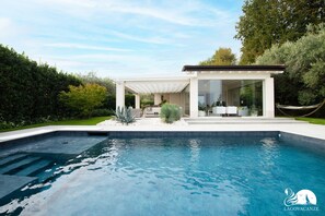 Una casa moderna con piscina, un porche cubierto y una hamaca.