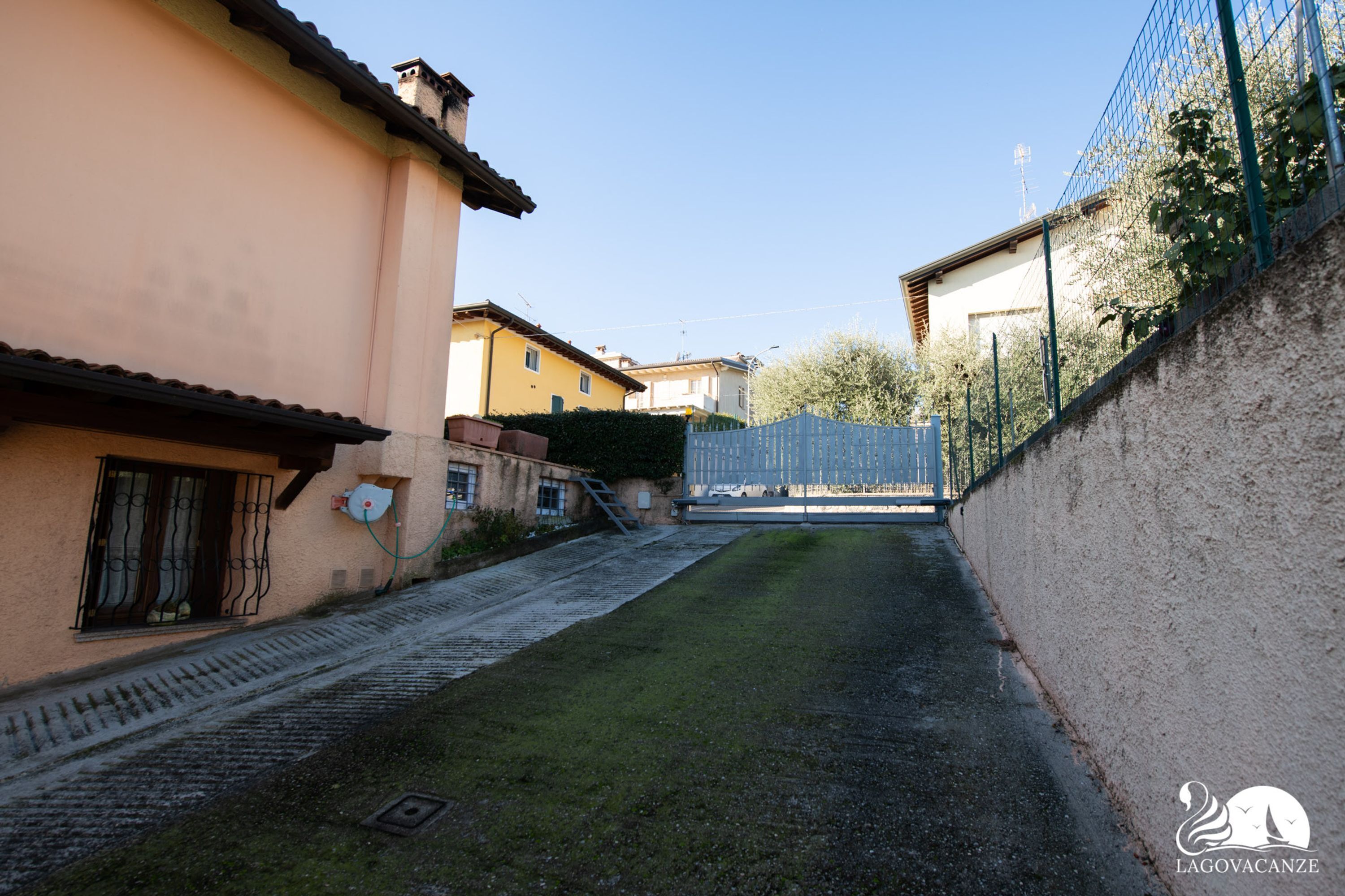 A narrow alleyway between buildings with a grassy area and a metal gate.