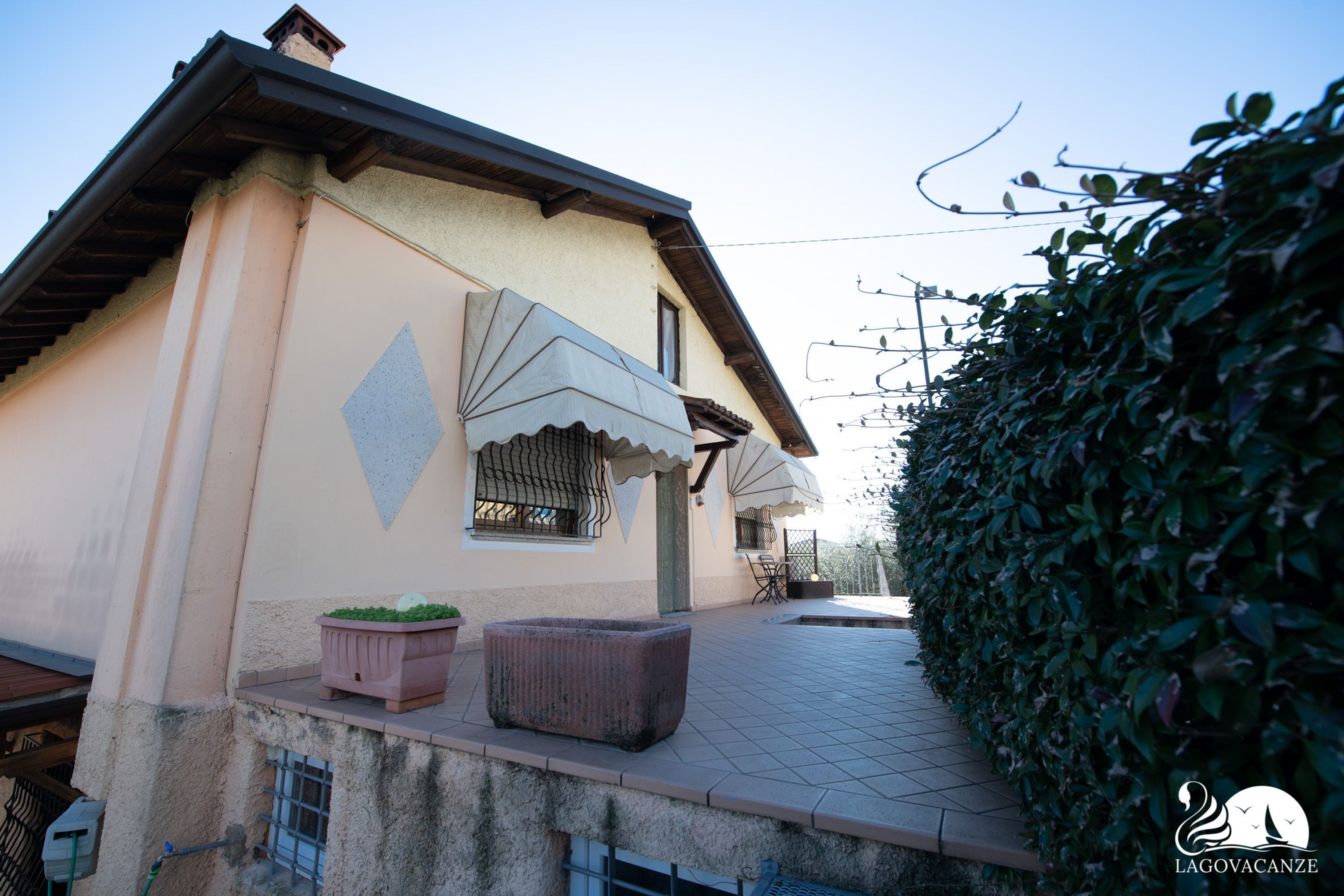 A building with a tiled patio, a large potted plant, and a hedge.