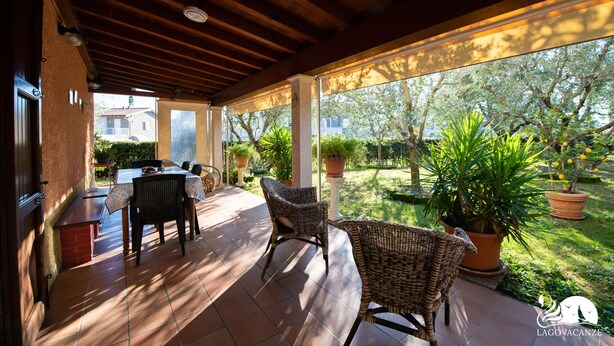 A covered patio with a table and chairs, potted plants, and a view of the surrounding garden. - Casa Celestina in Padenghe sul Garda (Padenghe sul Garda)