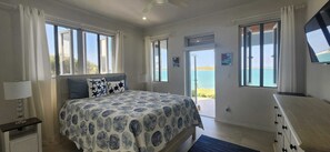 A bedroom with a bed, a nightstand, a dresser, and a view of the sea. - Private oceanfront home, 10 min drive to sandy beach
Beautiful SerenityBlu (Rolletown)