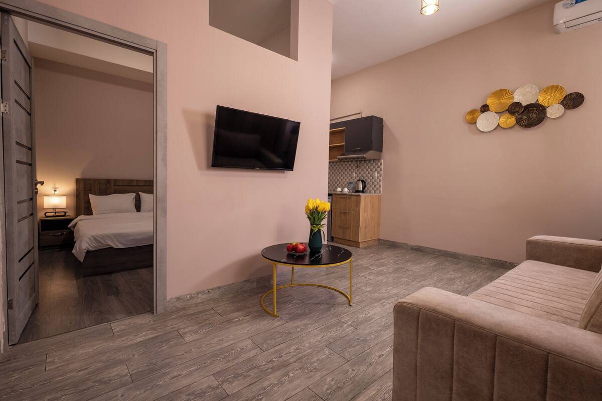 A modern hotel room with a bed, a TV, a small round table with flowers, and a sofa.
