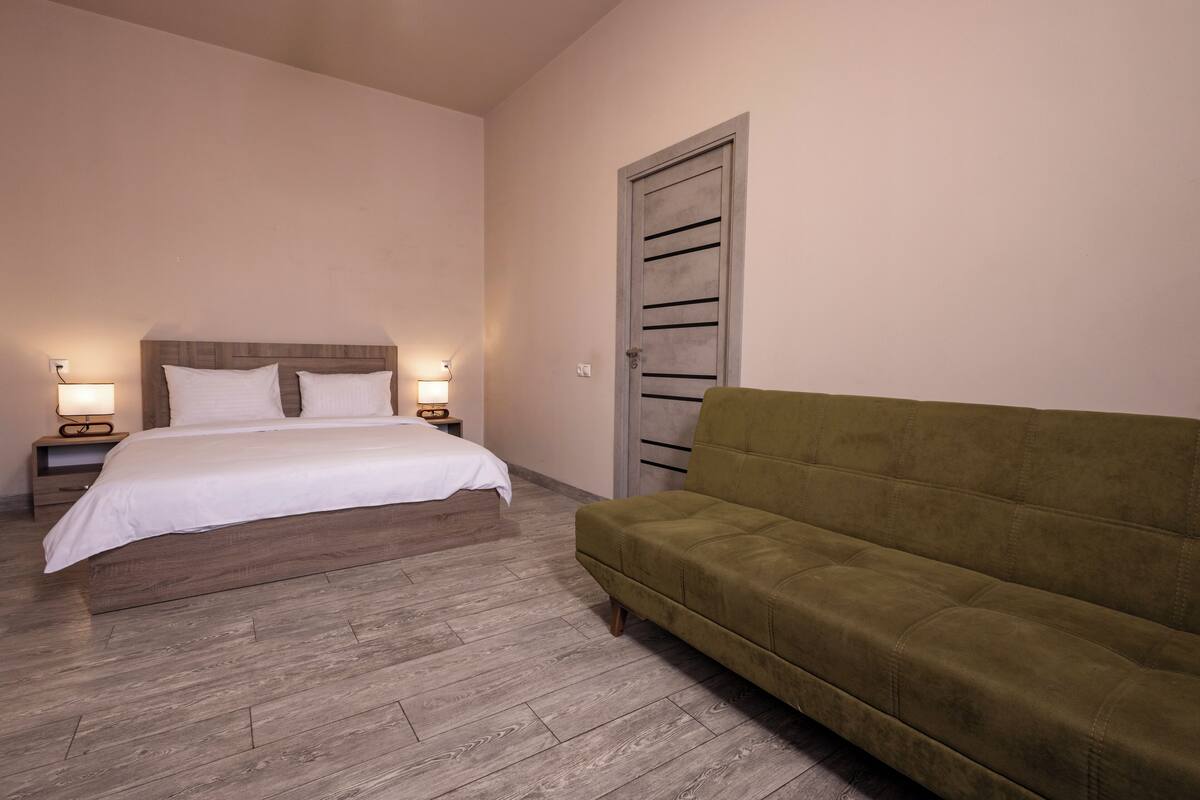 A bedroom with a bed, two bedside tables with lamps, a green sofa, and a door.