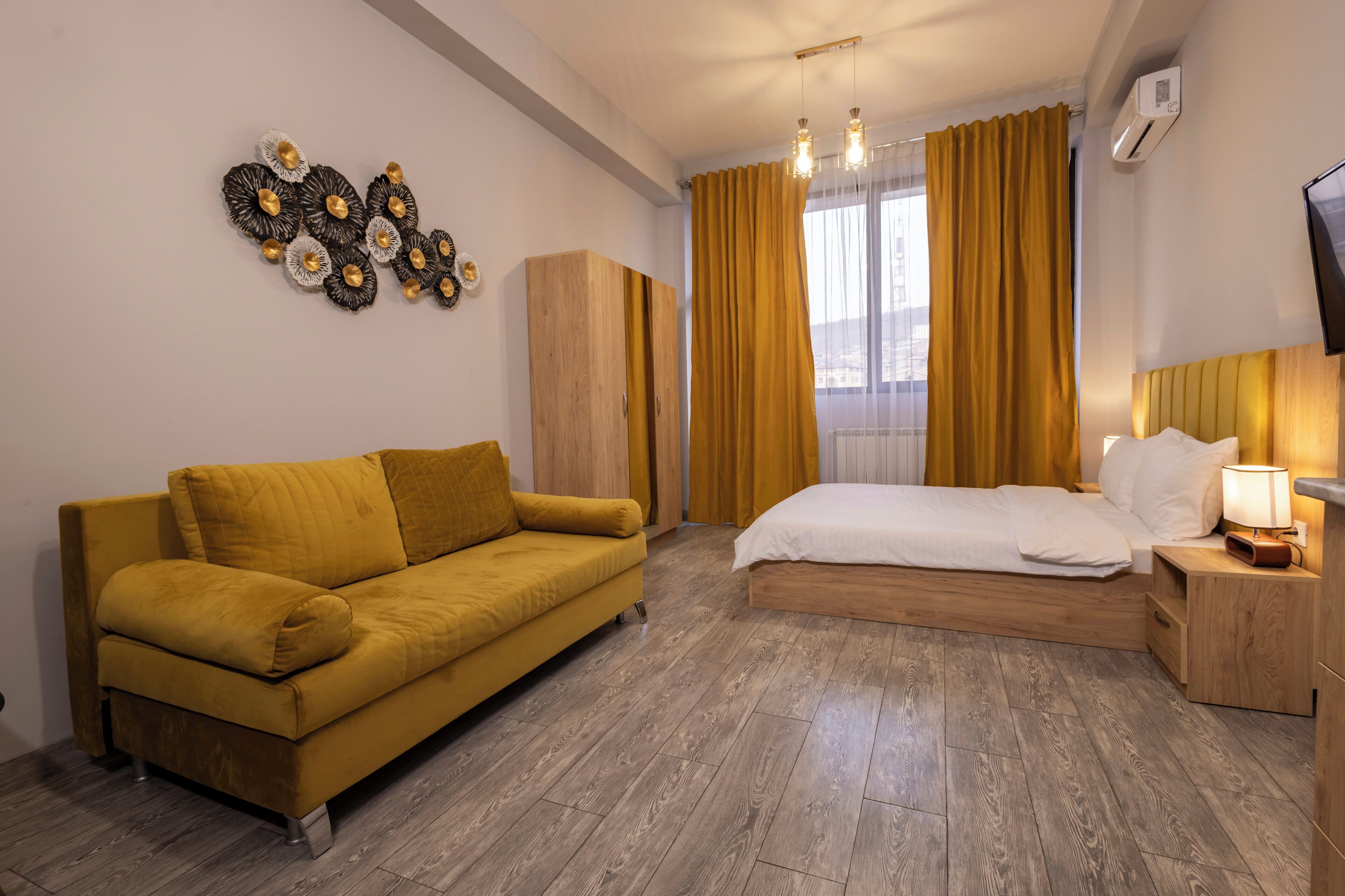 Habitación de hotel con piso de madera, un sofá, una cama, un armario y un televisor en la pared.