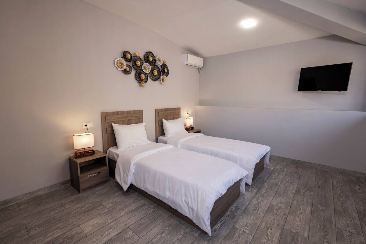 A hotel room with two beds, a flat-screen TV mounted on the wall, and a decorative wall piece above the beds.