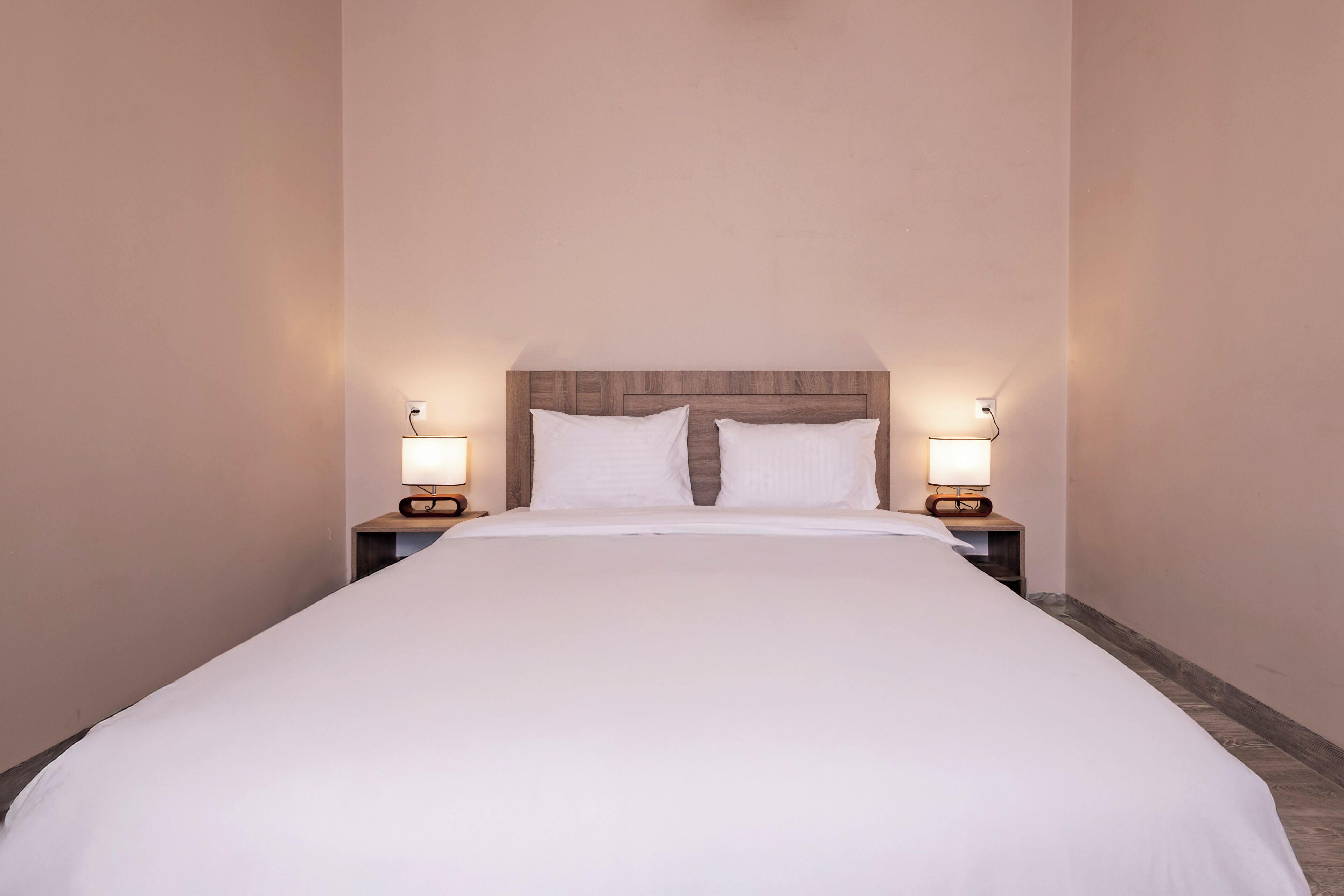 Una cama bien hecha con sábanas blancas, dos lámparas de noche y un cabecero de madera.