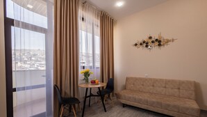 A living room with a sofa, a dining table with chairs, a vase of flowers, and a view through a large window. - Horizon Hotel Yerevan (Yerevan)