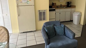 A compact kitchen with a refrigerator, microwave, and stove. There is a trash bin and a wicker chair in the living area. - Quaint 1 bedroom with a great view! Walking distance to everything! (Clearwater)
