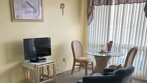 A living room with a television, a glass table, wicker chairs, and a sofa. - Quaint 1 bedroom with a great view! Walking distance to everything! (Clearwater)