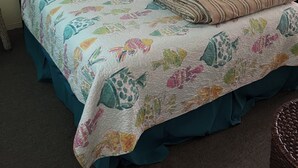 A bedroom with a bed, teal bedding, a framed picture on the wall, and a dresser with a lamp. - Quaint 1 bedroom with a great view! Walking distance to everything! (Clearwater)