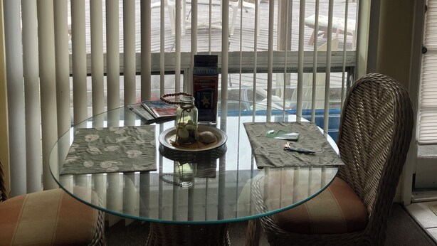A room with a glass table, wicker chairs, a view of a marina, and a window with vertical blinds. - Quaint 1 bedroom with a great view! Walking distance to everything! (Clearwater)