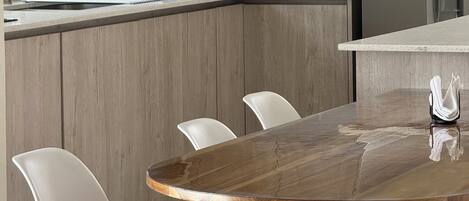 Eine moderne Küche mit Holzschränken, einem Edelstahlkühlschrank, einer Kaffeemaschine und einem runden Holztisch mit weißen Stühlen.