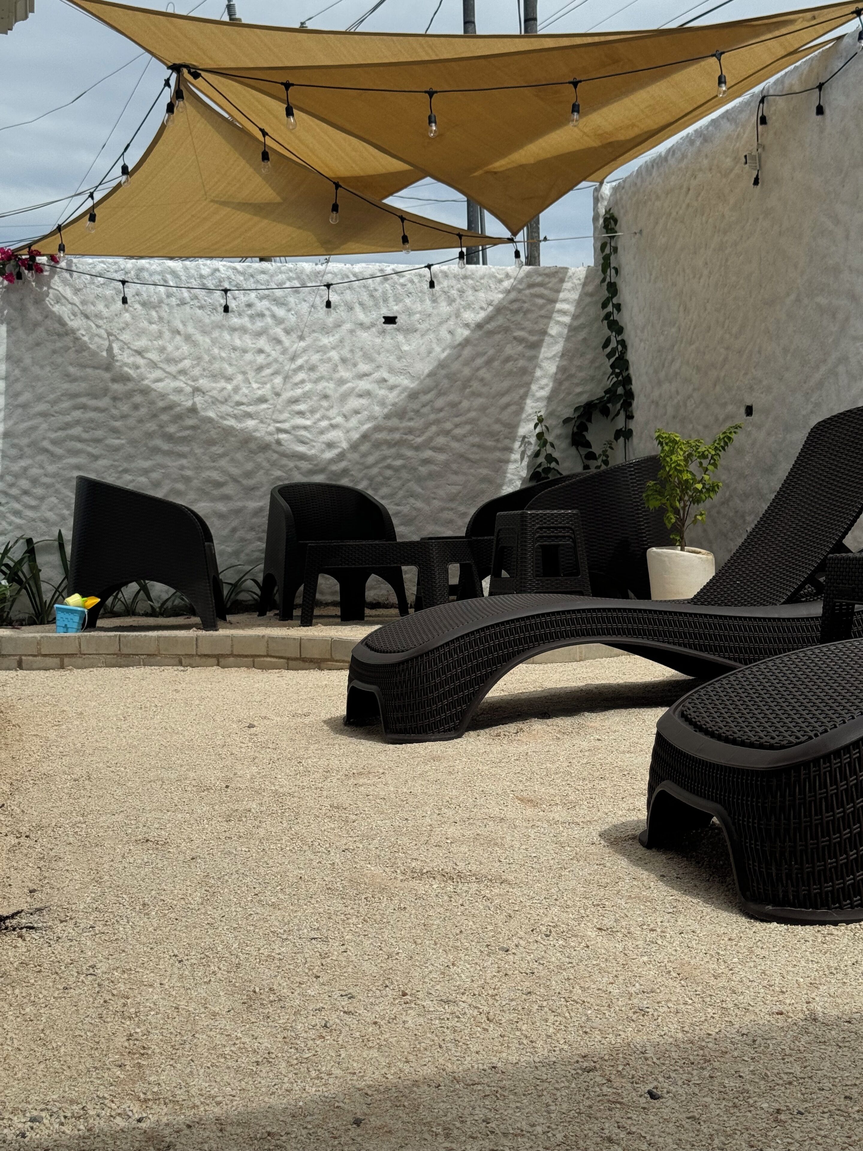 A covered outdoor seating area with black wicker furniture, a potted plant, and string lights.