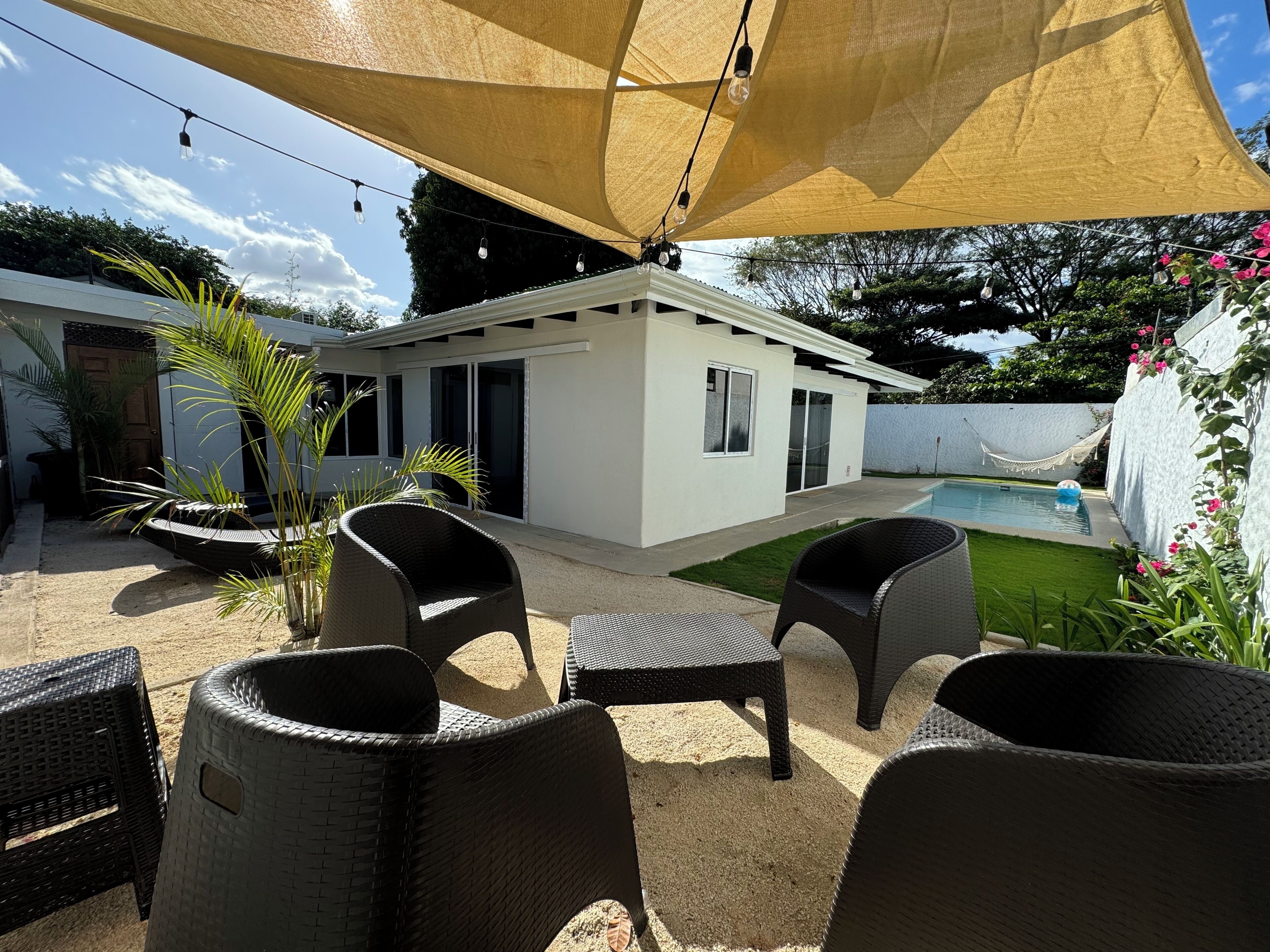 A covered outdoor area with wicker furniture, a pool, and a white building with sliding doors.