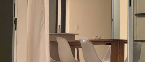 A modern dining area with a wooden table and white chairs, a hanging light fixture, and a white curtain.