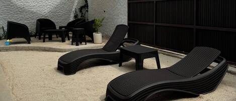 Un espace patio aménagé avec du mobilier d’extérieur, notamment des chaises longues et une table, placé sous une pergola.